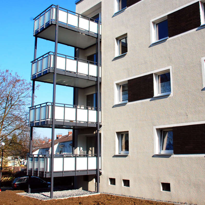 Das Bild zeigt einen Wohnblock mit nachträglich angebrachten, großzügigen Balkonen