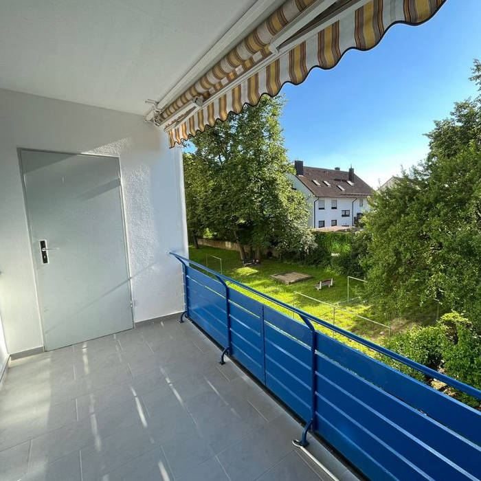 Das Bild zeigt den Balkon der sanierten Wohnung mit Blick in den gemeinschaftlichen Garten, das Geländer wurde frisch in Blau gestrichen.