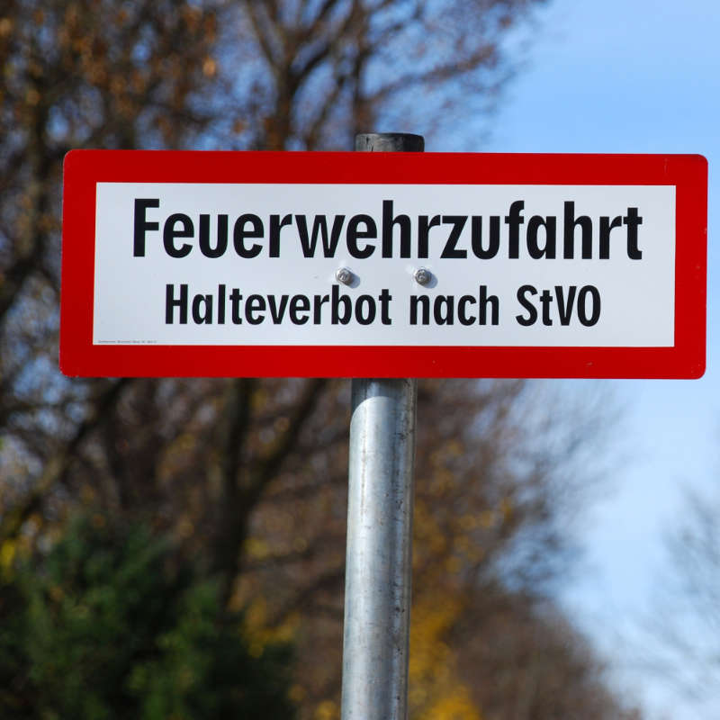 Das Bild zeigt ein vor einer Wohnanlage angebrachtes Verkehrszeichen mit der Aufschrift: Feuerwehrzufahrt